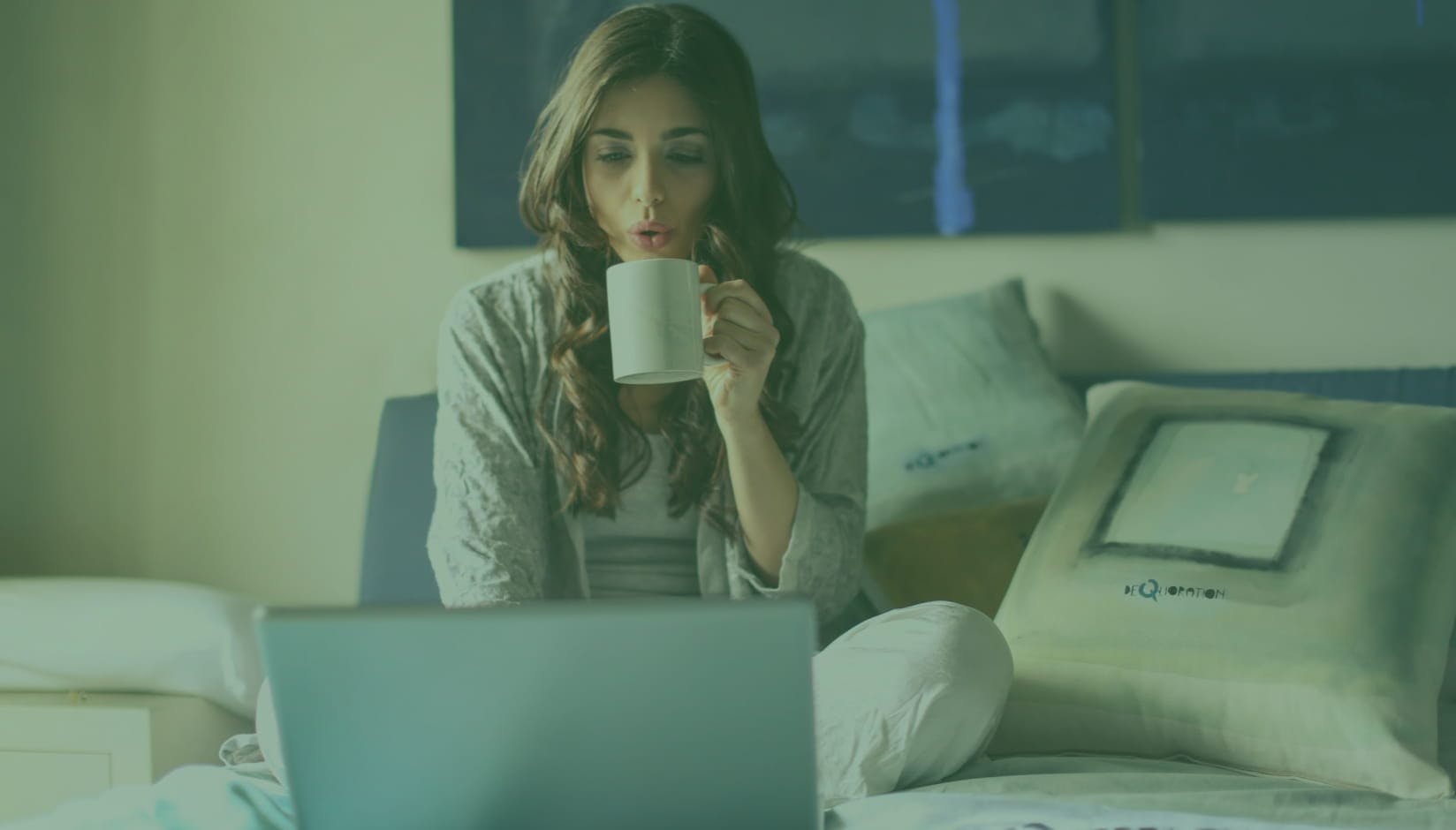girl coworking space member sitting on the bed at home with a laptop and a cup